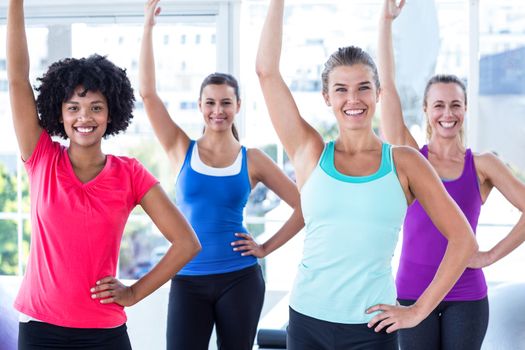 Portrait of women lifting one arm and smiling in fitness studio