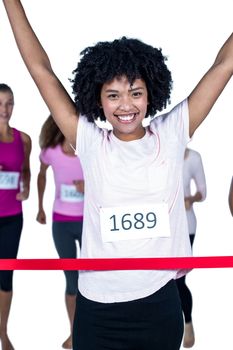 Portrait of happy winner female athlete crossing finish line with arms raised against white background