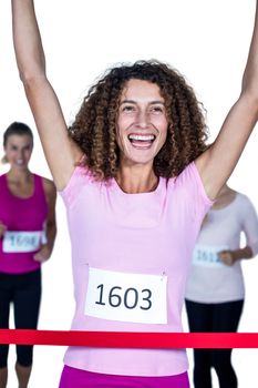 Smiling winner female athlete crossing finish line with arms raised against white background