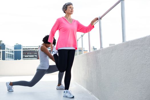 Mature woman exercising with female friend by railing outdoors