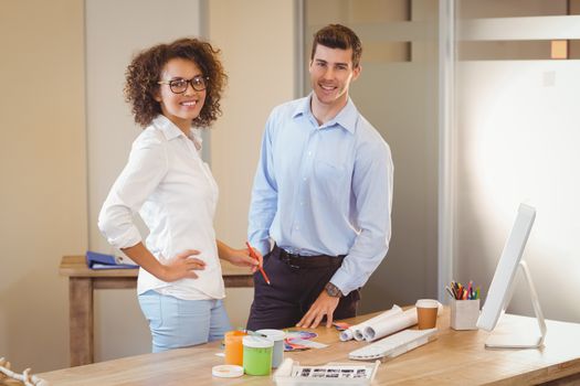 Portrait of smiling business people standing by table in office
