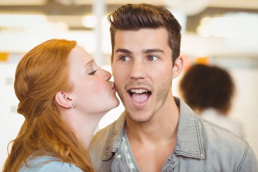 Woman kissing shocked businessman in creative office