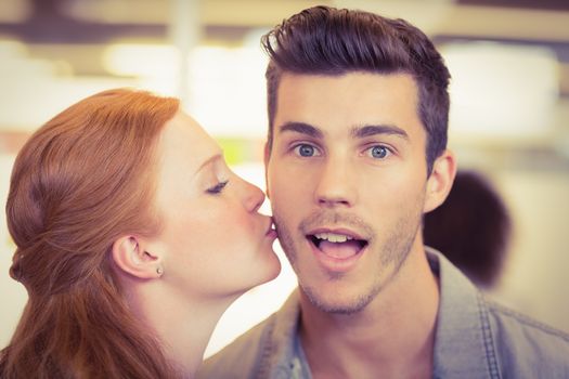 Portrait of shocked businessman being kissed by woman in creative office