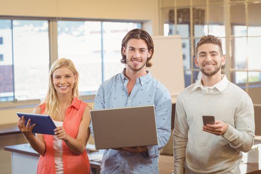 Portrait of smiling business people using various technologies in creative office