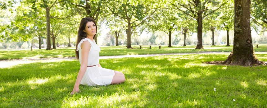 Panoramic view of park while young woman sitting on grassland