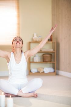 Full length of smiling woman meditating with arms raised and looking up while sitting on floor