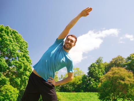 fitness, sport, training and lifestyle concept - smiling man stretching hand outdoors