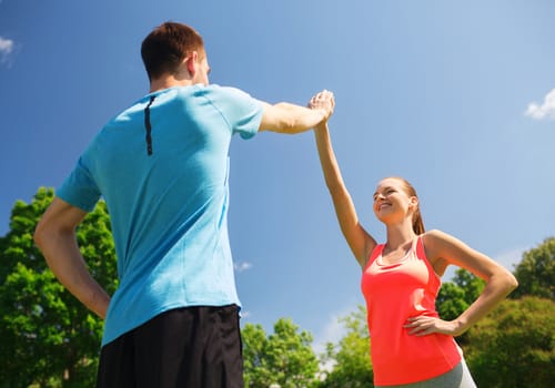 fitness, sport, training and lifestyle concept - two smiling people making high five outdoors