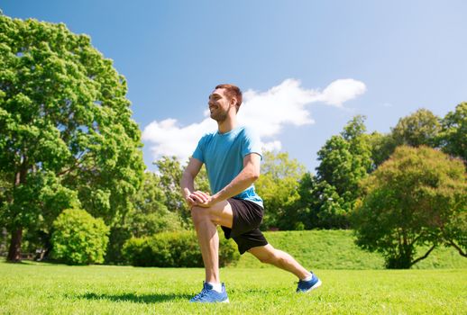fitness, sport, training and lifestyle concept - smiling man stretching leg outdoors