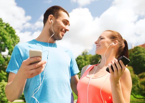 fitness, sport, training, technology and lifestyle concept - two smiling people with smartphones and earphones outdoors