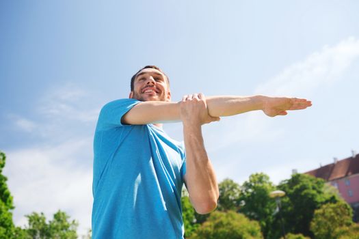 fitness, sport, training and lifestyle concept - smiling man stretching hand outdoors