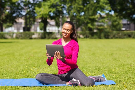 fitness, park, technology and sport concept - smiling african american woman with tablet pc computer sitting on mat outdoors