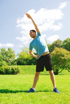 fitness, sport, training and lifestyle concept - smiling man stretching hand outdoors