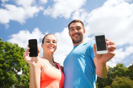 fitness, sport, training, technology and lifestyle concept - two smiling people with smartphones outdoors