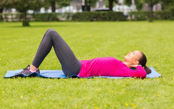 fitness, sport, training, park and lifestyle concept - smiling woman doing exercises on mat outdoors