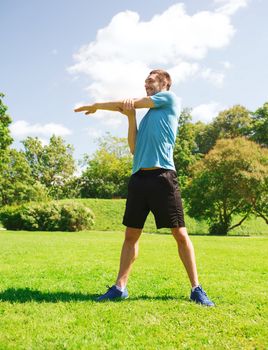 fitness, sport, training and lifestyle concept - smiling man stretching hand outdoors