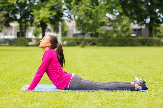 fitness, sport, training, park and lifestyle concept - smiling woman doing exercises on mat outdoors