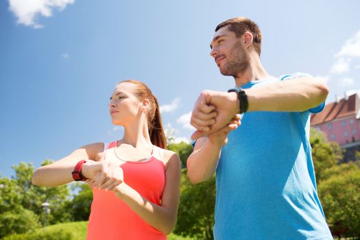 fitness, sport, training, technology and lifestyle concept - two smiling people with heart rate watches outdoors