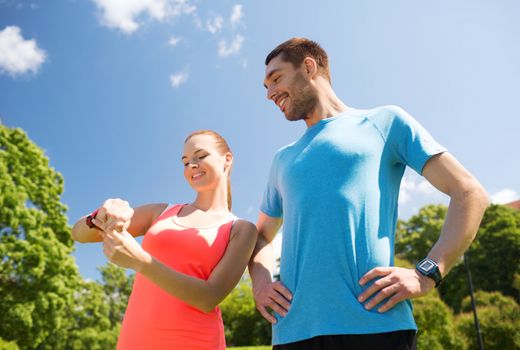 fitness, sport, training, technology and lifestyle concept - two smiling people with heart rate watches outdoors