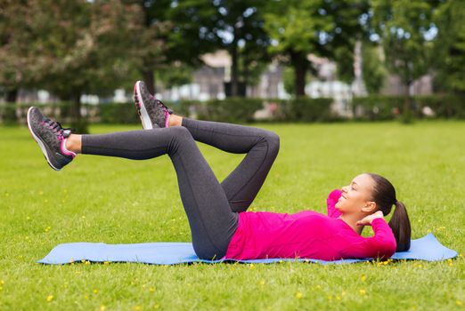 fitness, sport, training, park and lifestyle concept - smiling woman doing exercises on mat outdoors