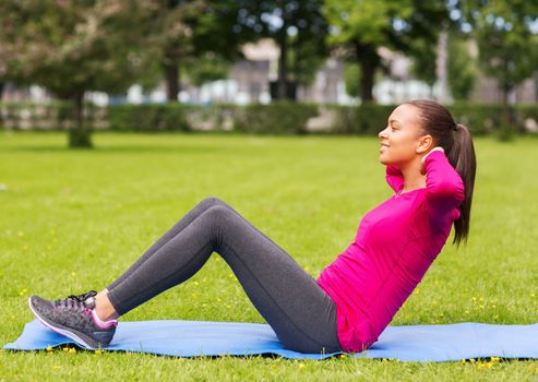 fitness, sport, training, park and lifestyle concept - smiling woman doing exercises on mat outdoors