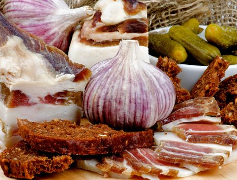 Homemade Raw Smoked Bacon with Brown Bread, Garlic and Gherkins closeup on Cutting Board