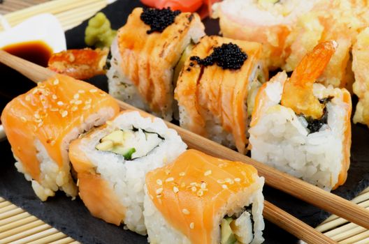 Arrangement of Various Maki Sushi with Smoked Salmon, Eel and Tempura Crab on Stone Plate closeup on Straw Mat background