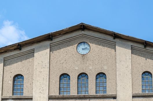 Factory building facade with clock in front of blue sky.
