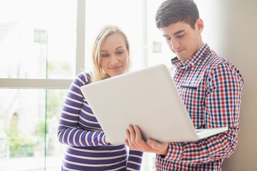  College students using laptop while standing by window