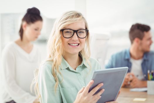 Portrait of happy woman wearing eyeglasses using digital tablet with people working at office