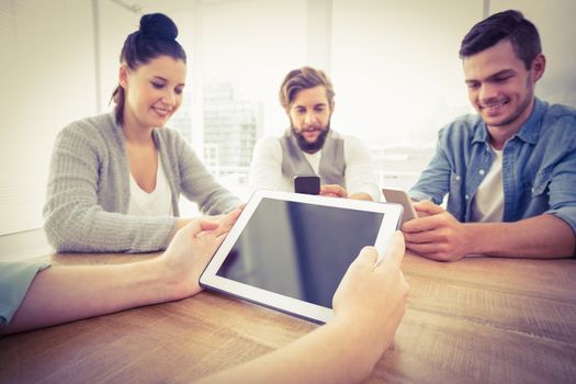 Cropped hand holding digital tablet with people using smartphones at office