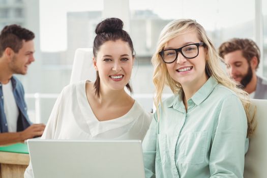 Portrait of smiling businesswomen working on laptop while sitting at desk in office