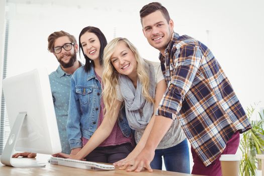 Portrait of smiling business people working at computer desk while standing in office