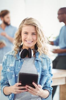 Portrait of happy woman with headphones while holding digital tablet in office