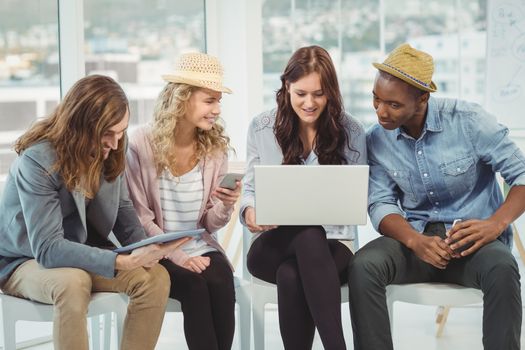 Smiling business people using technology while discussing in creative office