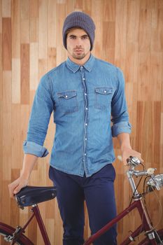 Portrait of hipster wearing knitted hat standing with bicycle against wooden wall