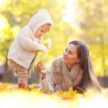 Mother and child having fun in autumn park among yellow leaves
