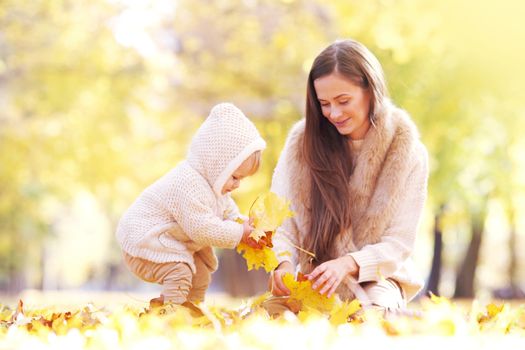 Mother and child having fun in autumn park among yellow leaves