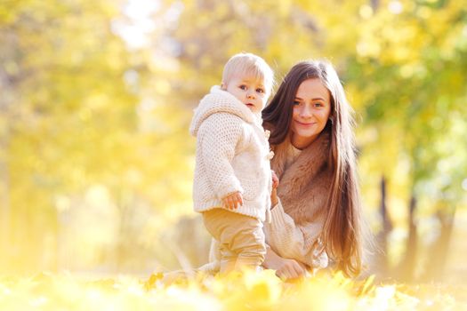 Mother and child having fun in autumn park among yellow leaves