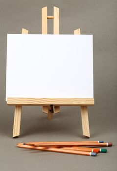 white paper, watercolor pencils and easel in grey background 