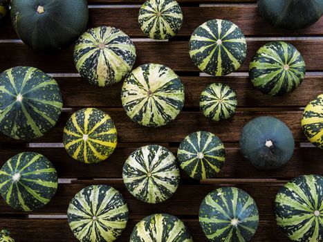 Still life with variety of green and yellow pumpkins cucurbita pepo spread on wooden table viewed from top, useable as seasonal autumn harvest Halloween housing decoration illustration