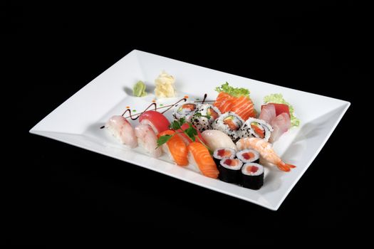 various sushi and sashimi with wasabi on white plate, black background