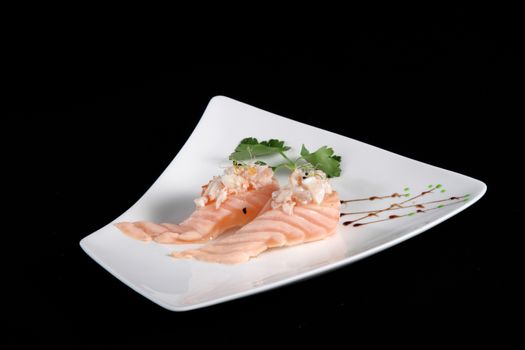 portion of sushi with vegetables on white plate, black background