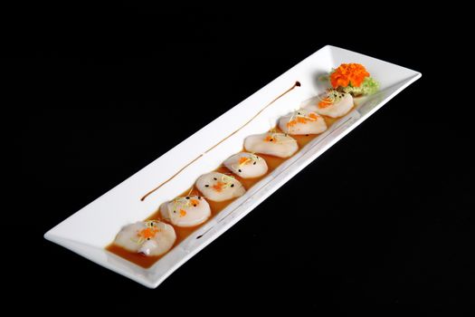 diced scallops with sauce on rectangular white plate, black background