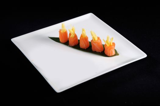 rolls of salmon on white plate, black background