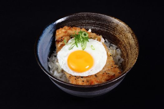 bowl with fried fish, rice and egg on a black background