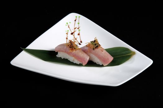 portion of sushi with vegetables on white plate, black background