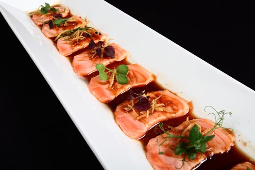 Salmon Steak with sauce and decoration of vegetables in white plate on a black background