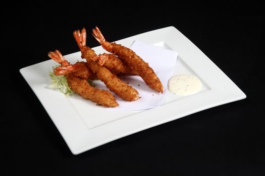 breaded prawns with vegetables and sauce in white plate on a black background