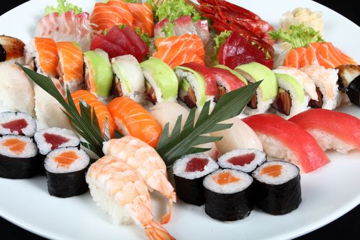 close-up sushi and sashimi mixed on round white plate on a black background